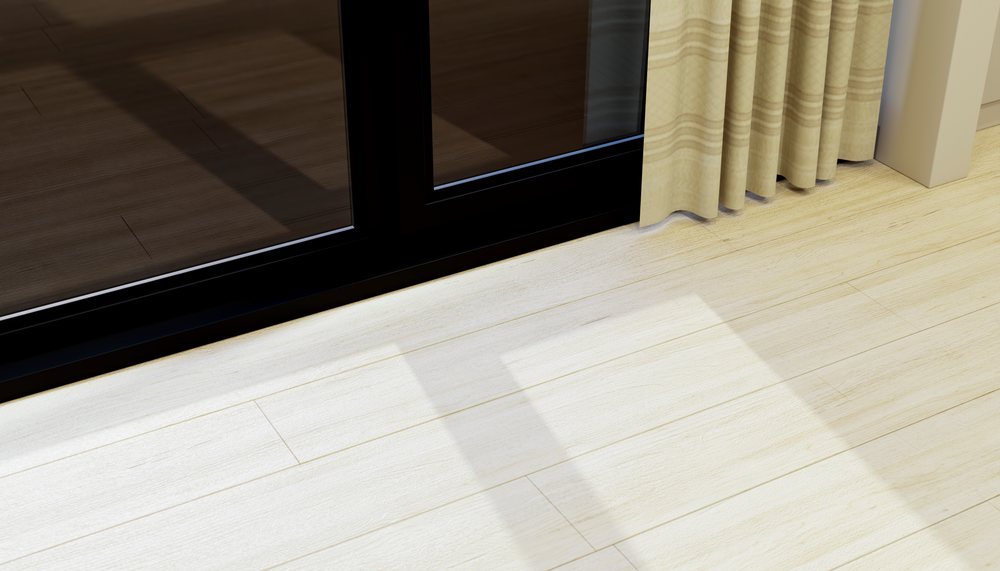 Light beige striped curtains cast shadows on a light wooden floor near a black-framed glass door in a modern home interior with natural light.