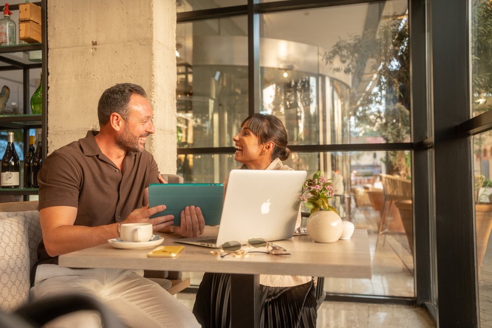 Two coworkers engage in a business meeting using a laptop and tablet at a modern cafe table, Seville, Andalucia.