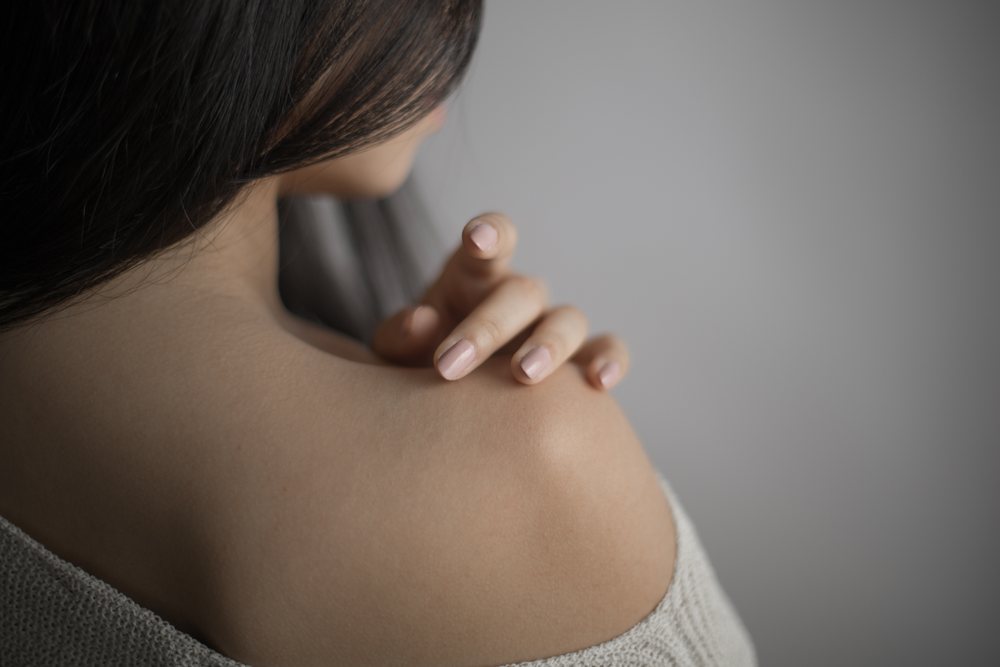 Woman with long hair gently touches her bare shoulder in a close-up portrait with soft lighting and a neutral background, Art, emotional.