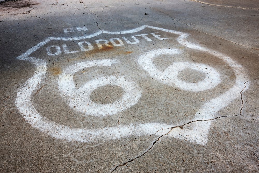 White Route 66 shield painted on cracked asphalt pavement in an outdoor Texas road environment, USA.