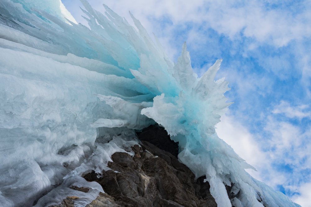 Frozen Waterfall, jagged frozen ice formations hang from a rocky cliff below a partly cloudy sky, Landscape, Nordkjosbotn, Norway.