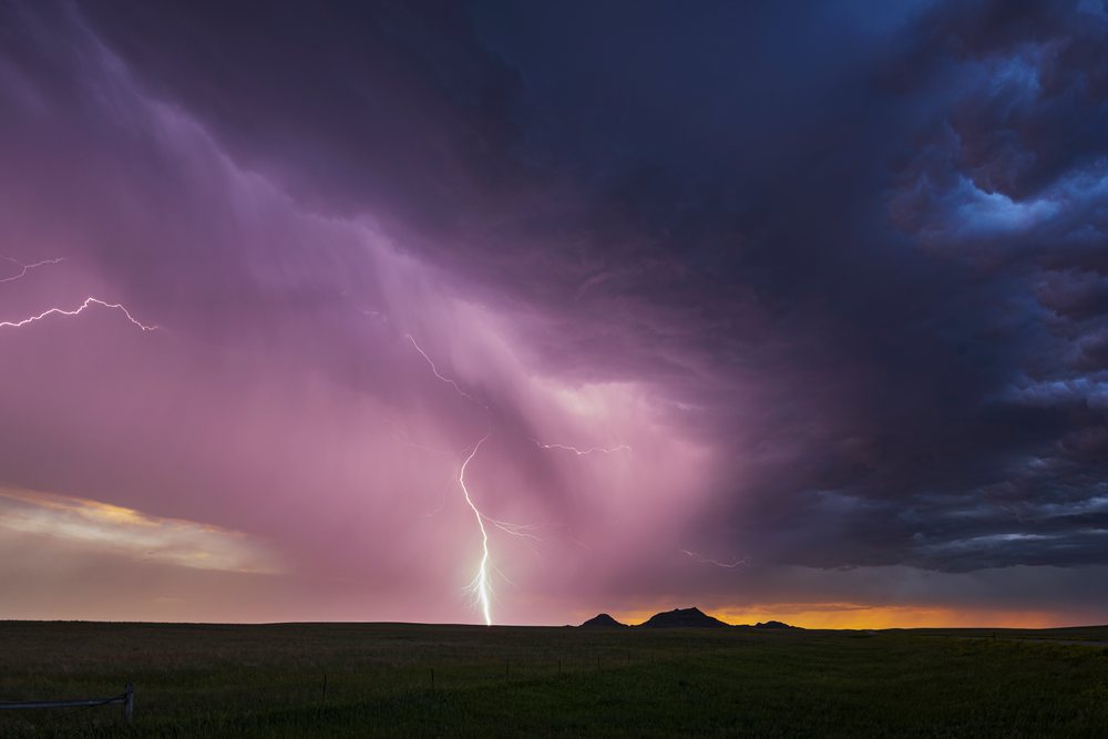 Lightning strike visible in dark storm clouds over open grassy plains, at sunset, Storm Chasing, Weather, Environmental Issues, Redig, South Dakota, USA.