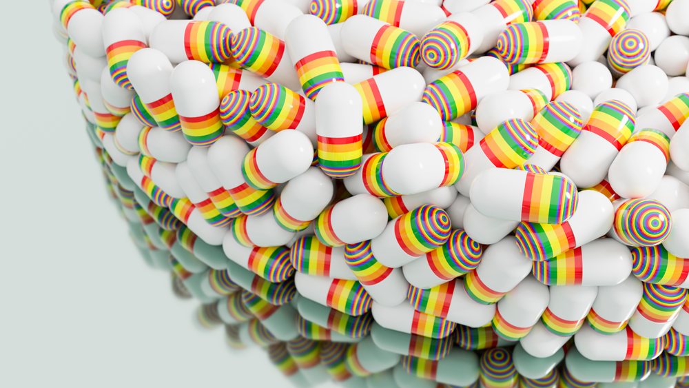 Close-up of white medicine capsules with rainbow stripes piled on a reflective surface.