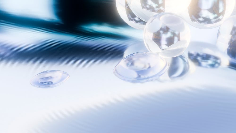 Transparent glass spheres clustered on a smooth reflective surface with water droplets and soft blue light reflections.
