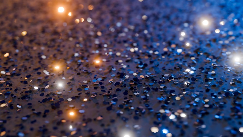 Blue glitter pieces scattered on a surface with glowing sparkles and light reflections creating a festive atmosphere.