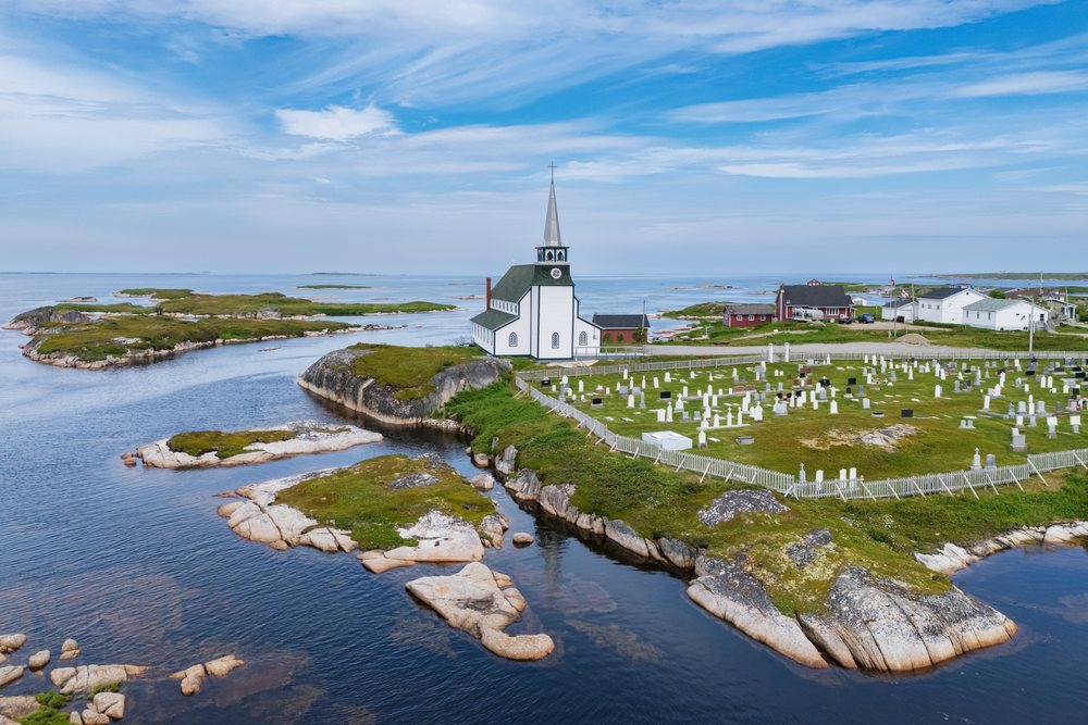 White wooden St Luke's Anglican Church with steeple beside fenced cemetery on rocky coastal land with islands, Landscape, Wildlife, Lifestyle, Newtown, Newfoundland & Labrador, Canada.
