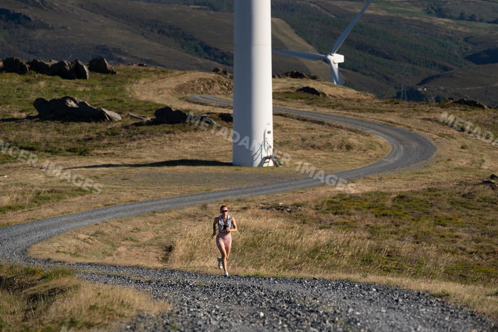 A white woman runs on a gravel trail by wind turbines in Galicia Spain