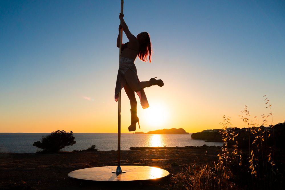 Silhouetted woman performing pole dance at sunset by the Ibiza coastline outdoors near the sea, Spain.