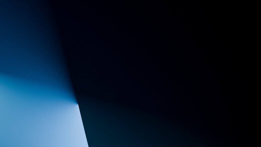 Corner of a wall illuminated by blue light contrasting with deep shadows in a dark interior.