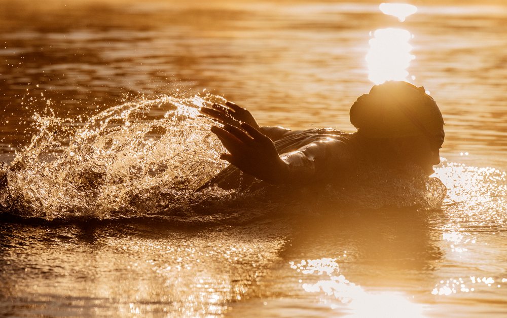 Person swimming outdoors at sunset with water splashing and golden light reflecting on the surface, USA.