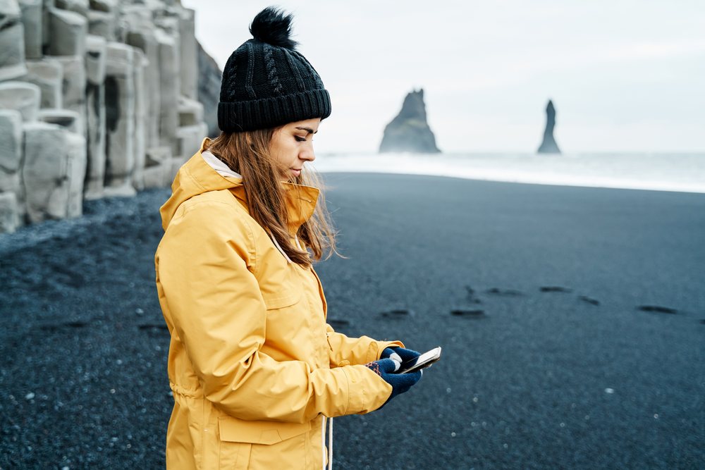 White Woman using smartphone on black sand beach in a beach