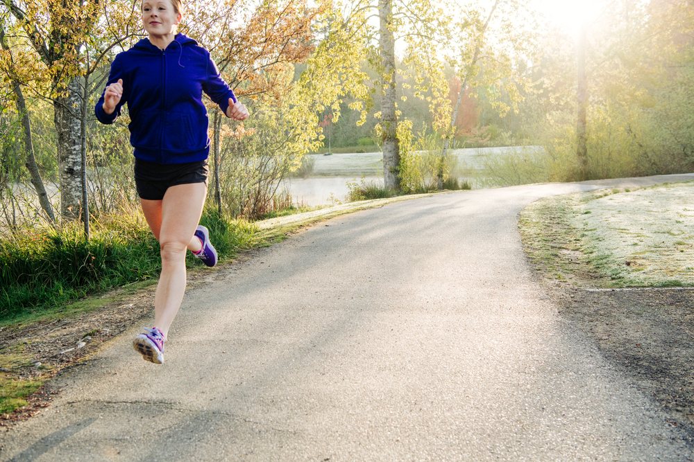 Woman running on a paved path in a morning park setting with trees and sunlight, Washington, Bainbridge Island, USA.