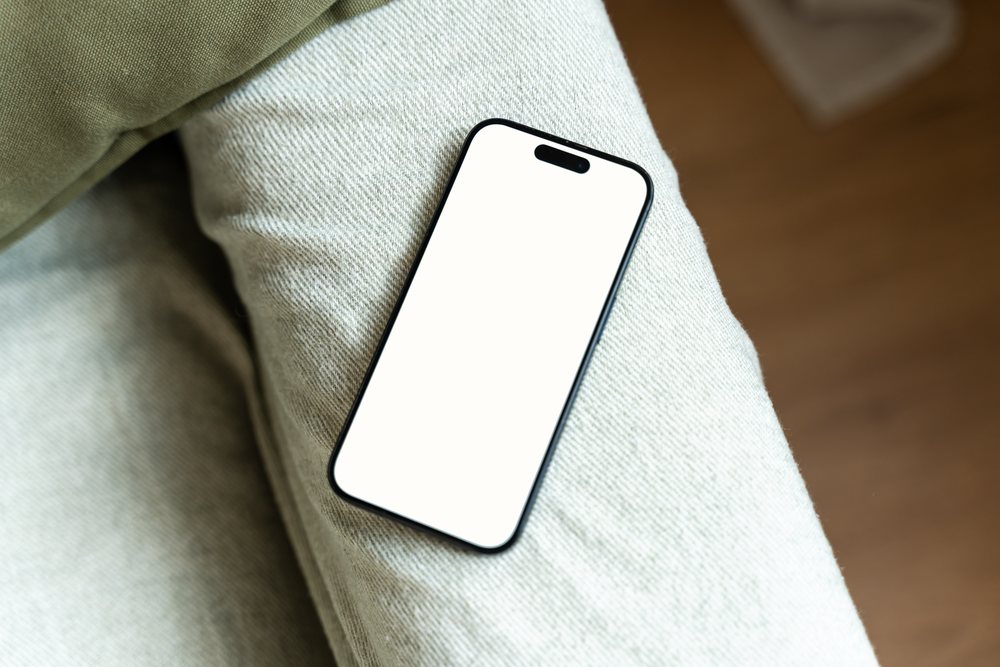 Smartphone with white screen lying on beige pants indoors, mock up, Spain.