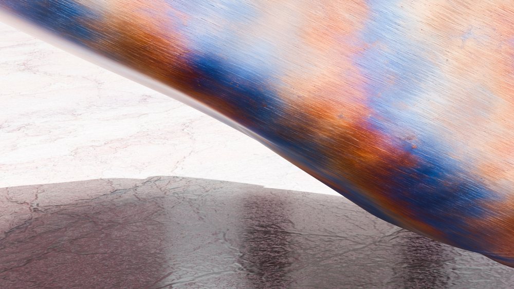 Close-up of a rusty, colorful oxidized metal surface showing blue and orange hues with textured corrosion and visible reflections.