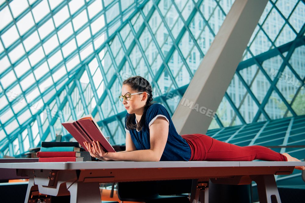 A young woman reads a book while lying on a table