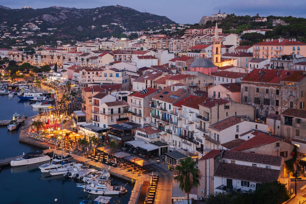 Boats docked at Calvi harbor at Dawn with illuminated historic buildings and a church bell tower, Travel Photography, Corsica, France.
