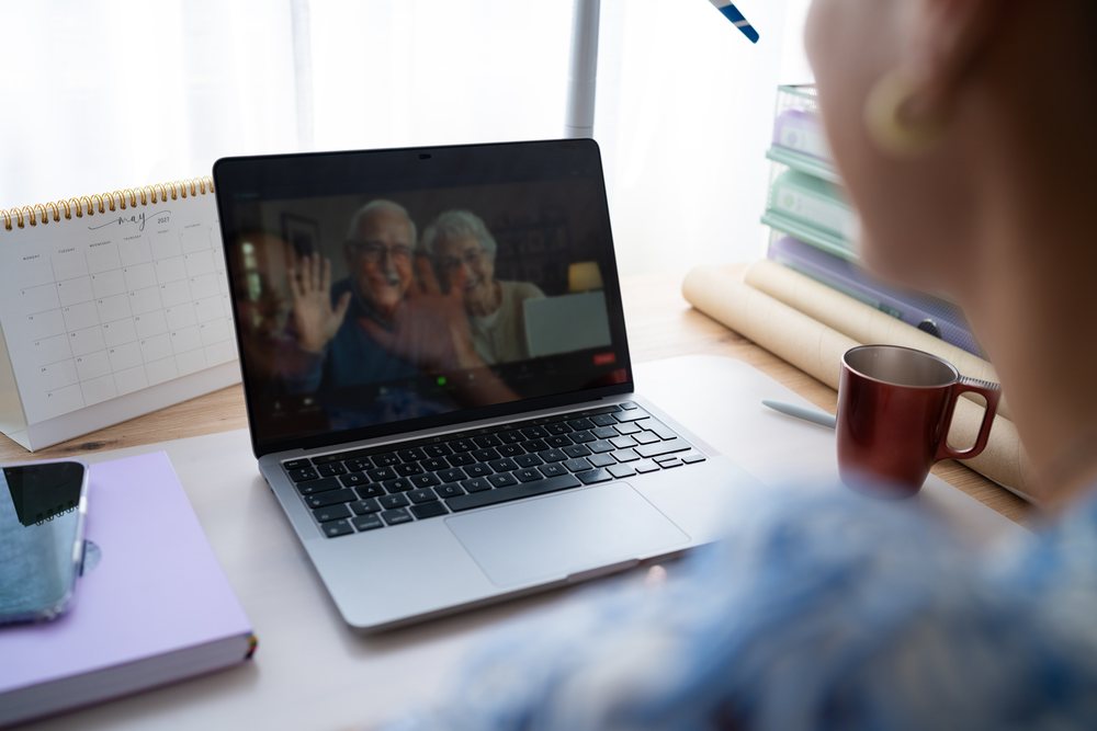 Person in a home office uses a laptop to video call an elderly couple waving on the screen, telecommuting, Spain.