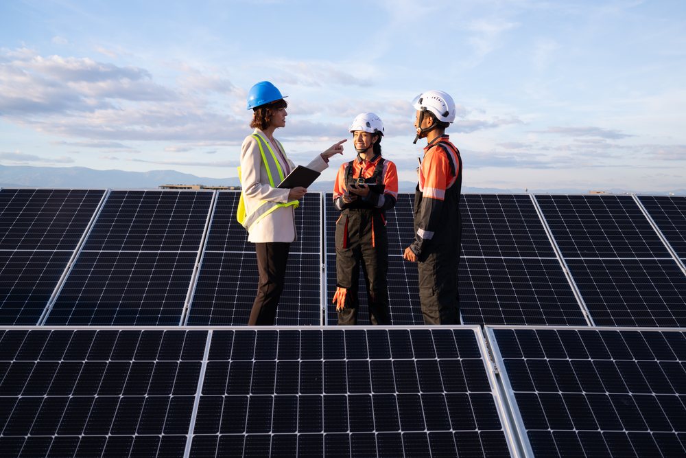 Three solar energy professionals discuss work at a solar panel installation outdoors, under a clear sky, Madrid, Spain.