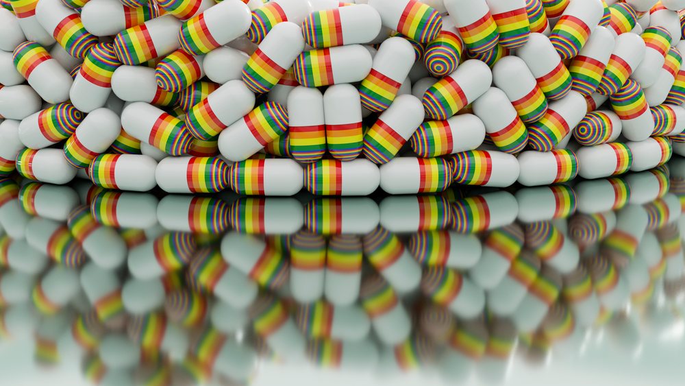 White capsules with rainbow stripes are stacked and scattered on a glossy surface creating colorful reflections.