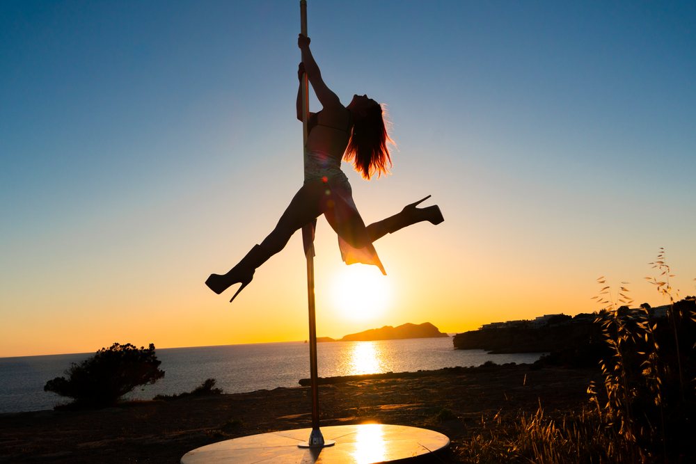 Silhouette of a woman performing a pole dance on a clifftop at sunset, with ocean and sky in the background, Ibiza, Spain.
