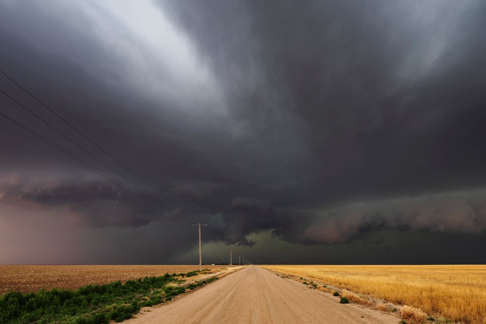 Developing Supercell storm over a county dirt road with power poles amid flat farmland, within Tornado Alley, Storm Chasing, Weather, Environment, Tribune, Kansas, USA.