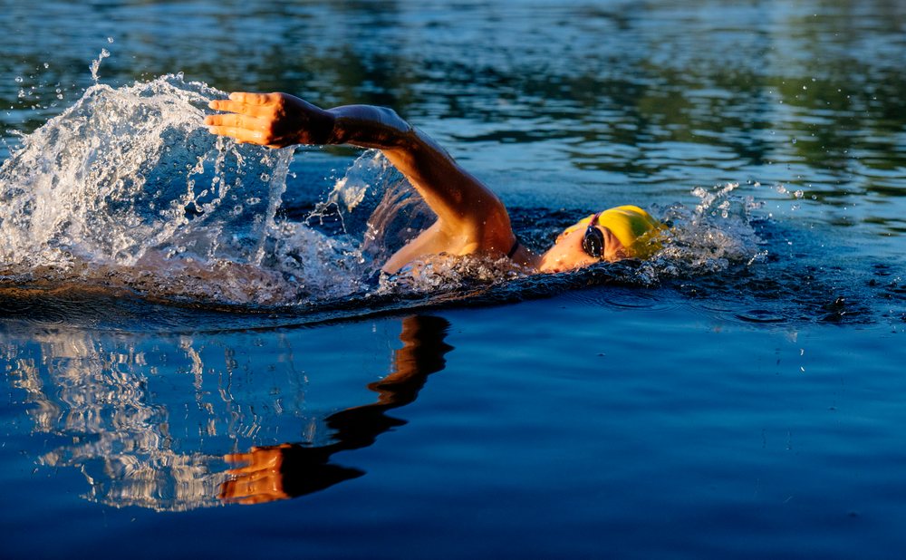 Swimmer performing freestyle stroke in open water wearing a yellow swim cap and goggles, USA.