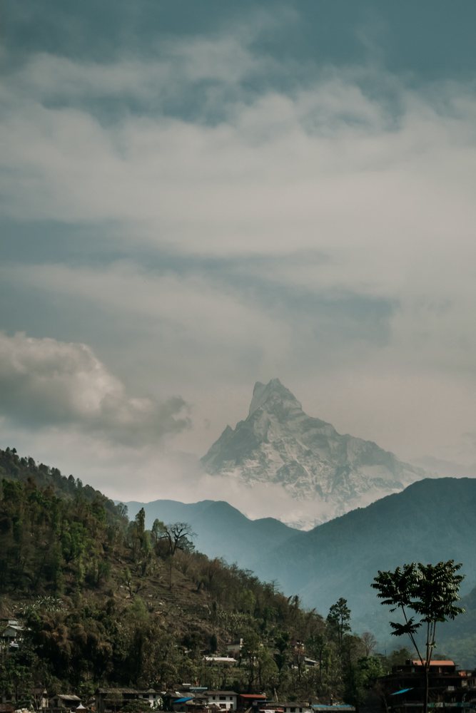 Mountain peak towering above forested hills and a village with clouds scattered across the sky, mountaineering, climbing, landscape, Nepal.