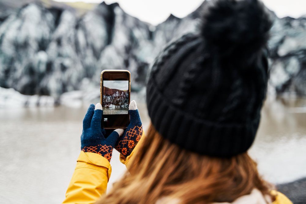 A white person photographs a glacier mountain landscape over a lake