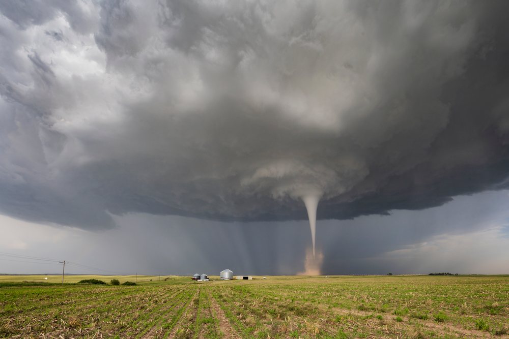 Tornado spinning beneath a dark storm cloud over rural farmland with grain silos, Dickens, Nebraska, USA.