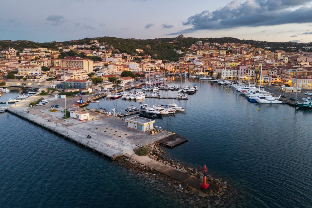 Dawn over the harbor, showing boats moored by a pier with hillside town in the background, Travel Images, La Maddalena, Sardinia, Italy.