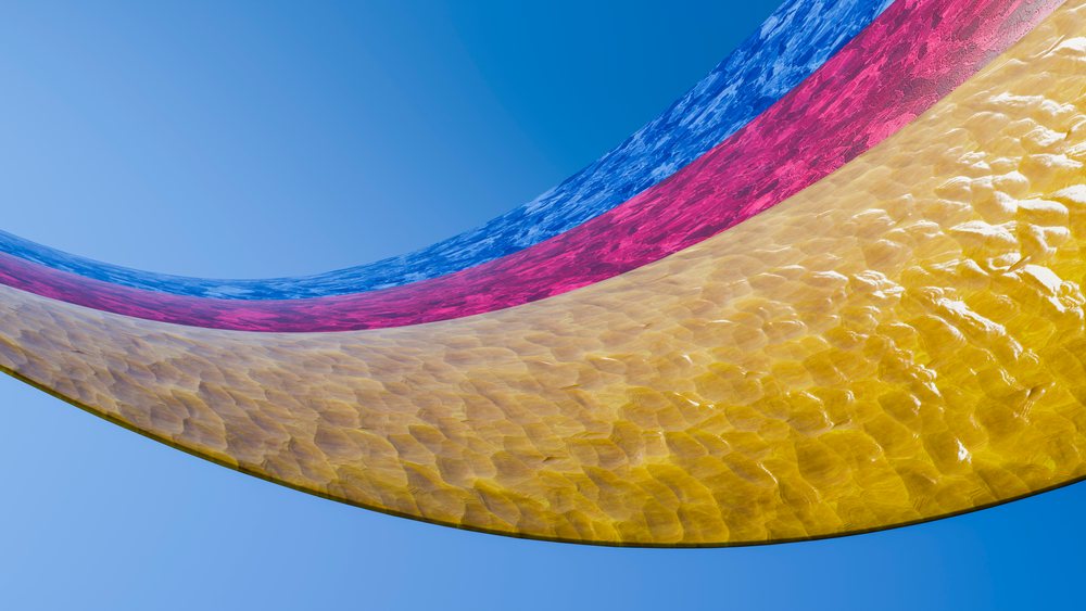 Three curved blue, red, and yellow translucent water sheets flow with ripples against a clear blue sky.
