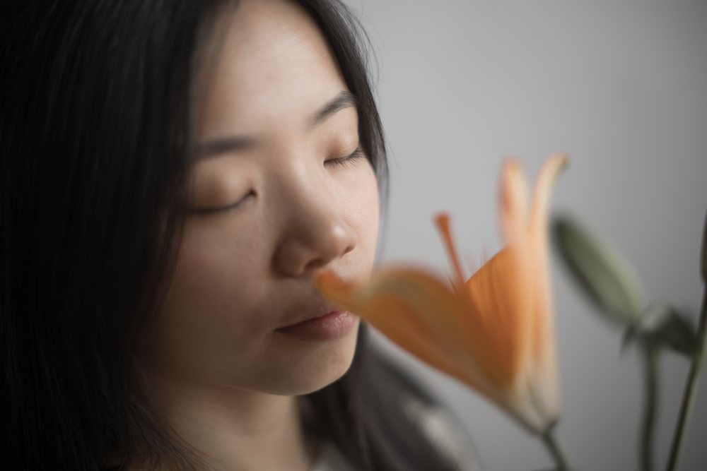 Woman with closed eyes smells an orange lily flower indoors in a calm, serene setting, Art, portrait, emotional.
