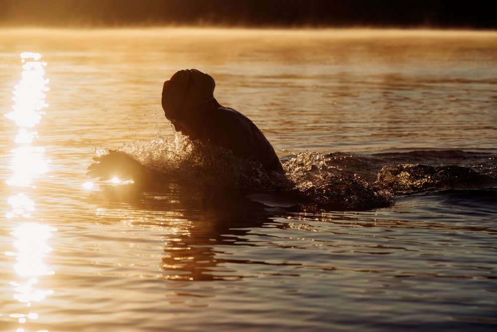 Swimmer wearing a cap swimming in a lake at sunrise with visible water splashes, USA.