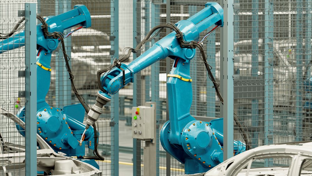 Two blue robotic arms assemble a metal car frame inside an industrial automated assembly line at a manufacturing plant.