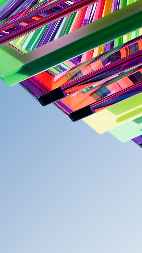 Colorful transparent acrylic panels arranged in overlapping geometric shapes reflect light against a clear blue sky.