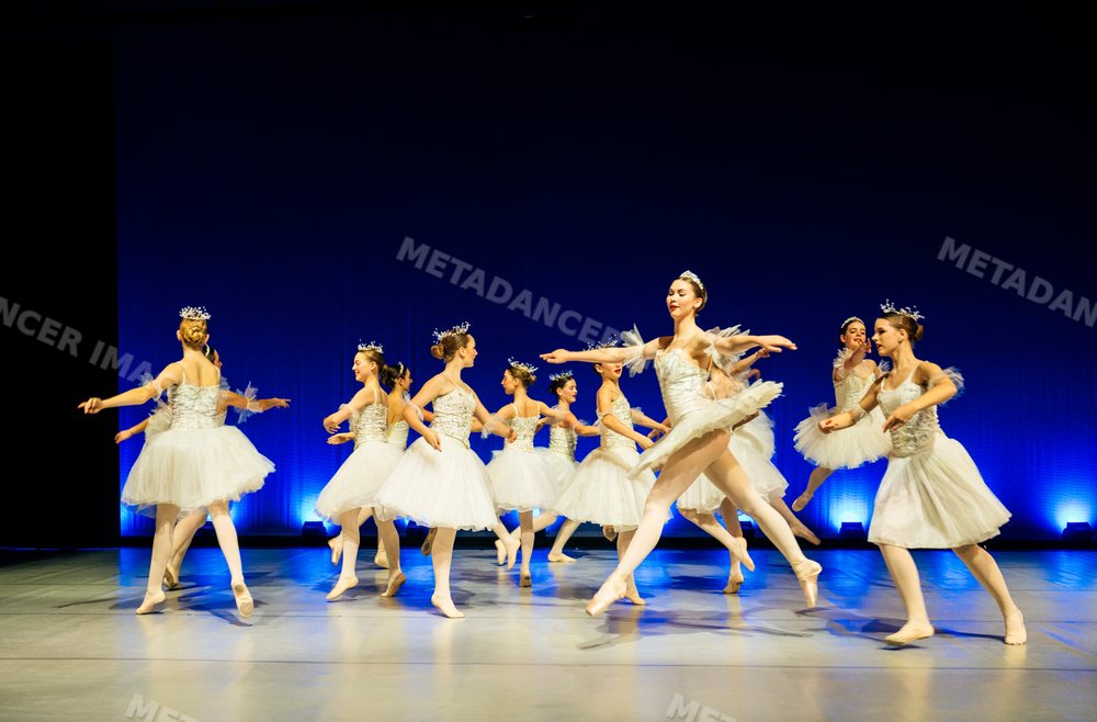 Female ballet dancers in white tutus perform on stage during a ballet