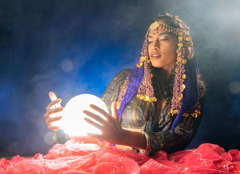 A fortune teller woman in ethnic clothing holds a glowing crystal ball with a smoky background in the, USA.