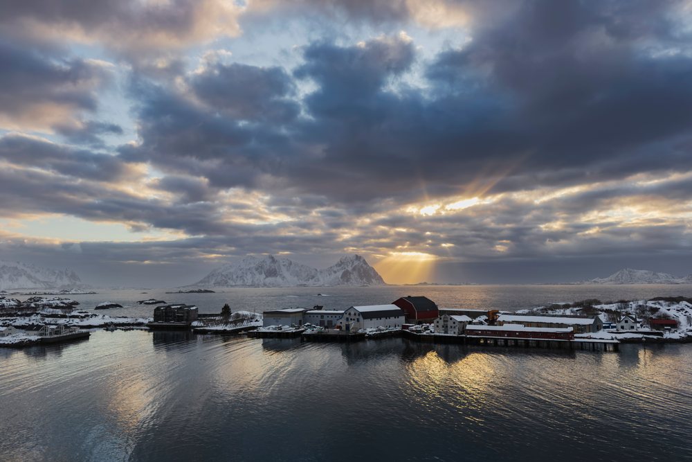 Sunrise east of Svolvaer, shows snowy mountains, calm sea, and dramatic clouds lighting the sky, Landscape, Lofoten, Norway.