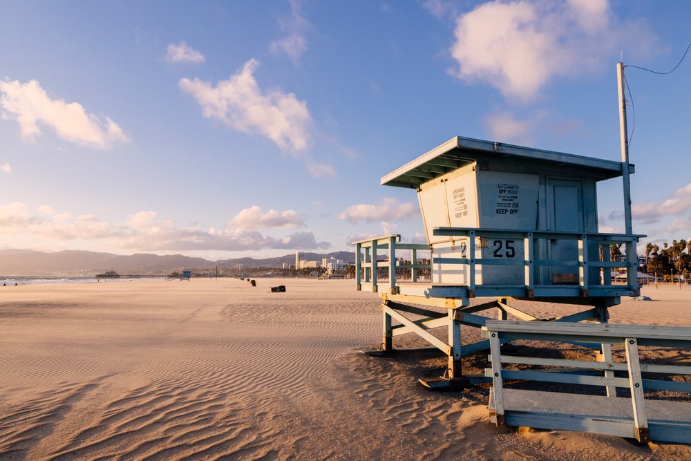 Lifeguard tower 25 stands on the sandy Venice Beach, California, under a partly cloudy sky at sunset, USA.