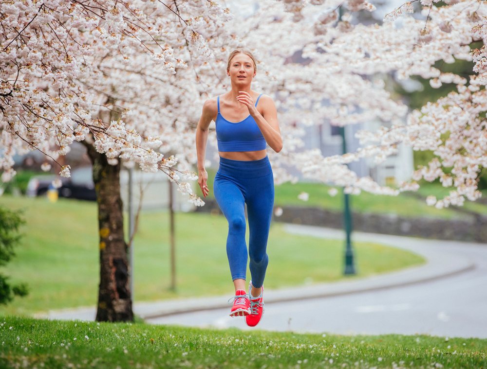 Woman running energetically on a grassy path under cherry blossom trees in a park, USA.