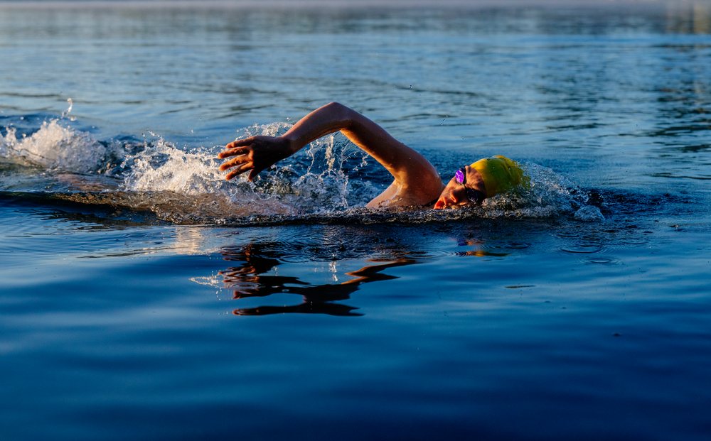 Swimmer wearing a yellow cap and goggles performing freestyle stroke in a calm lake, USA.