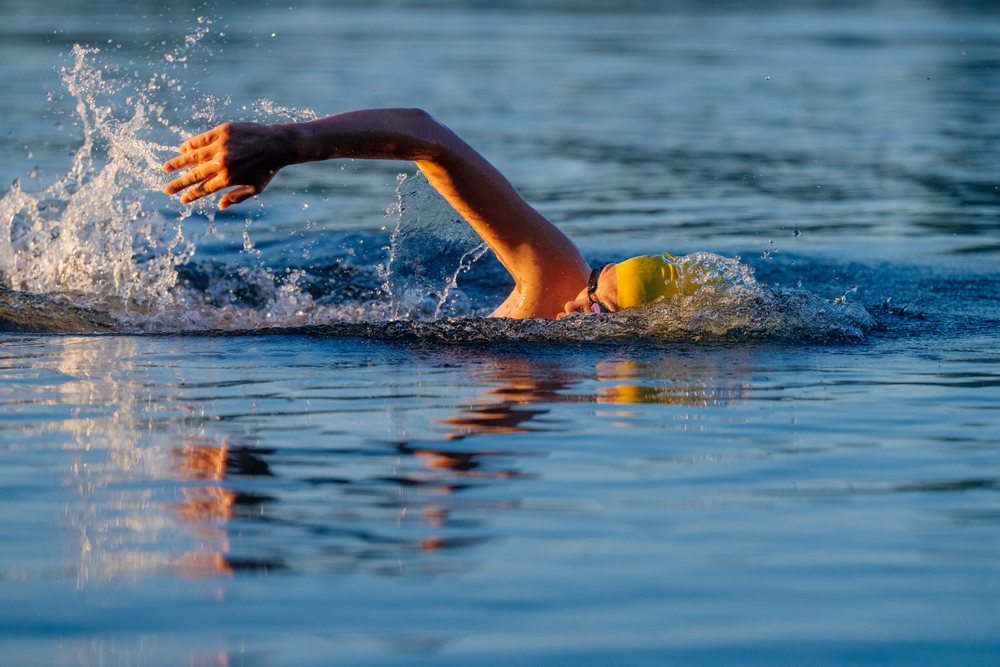 Swimmer wearing a yellow swim cap and goggles performing freestyle swimming in open water, USA.