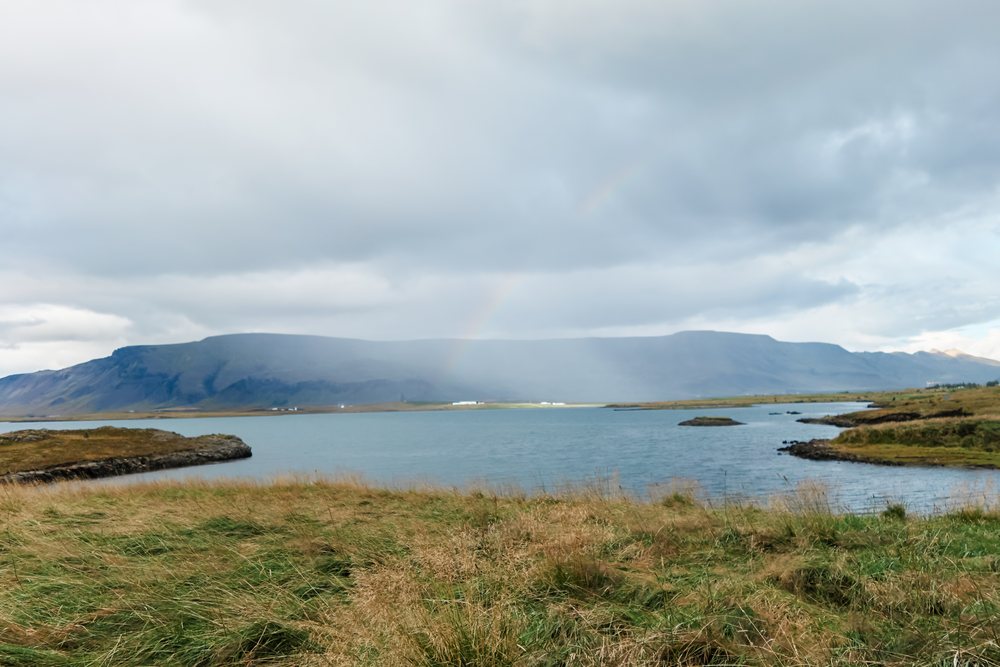 A rainbow appears over a lakeside mountain landscape