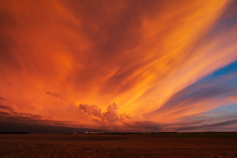 Orange and blue sunset sky with large clouds over flat rural plains and grain storage silos, Storm Chasing, Weather, Environmental, Winner, South Dakota, USA.