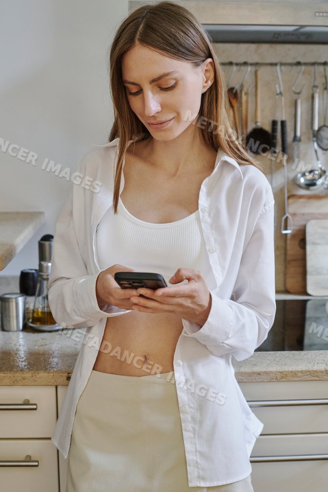 Young white woman using smartphone in a modern kitchen in a kitchen