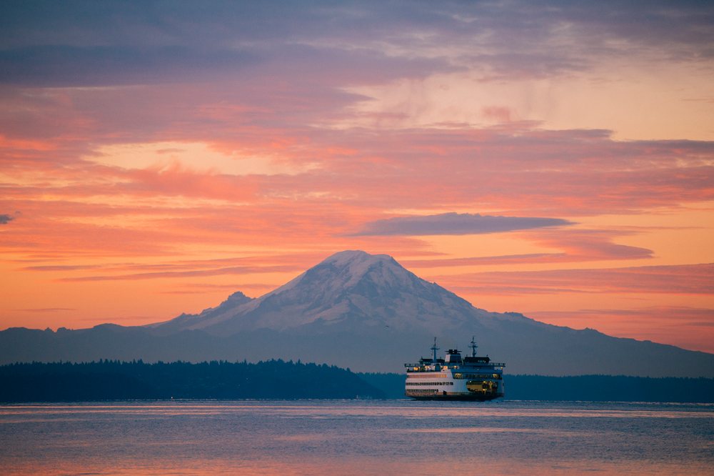 Ferry crosses calm Puget Sound at sunset with Mount Rainier visible in the background, Bainbridge Island, WA, USA.