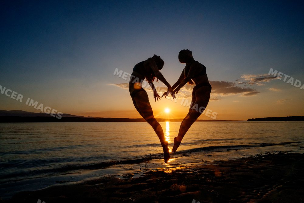 Two white people doing partner acrobatics jumps on a beach at sunset