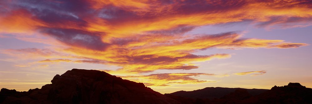 Sunset lighting silhouettes rock formations's Valley of Fire State Park beneath colorful clouds in a desert landscape, Nevada, USA.