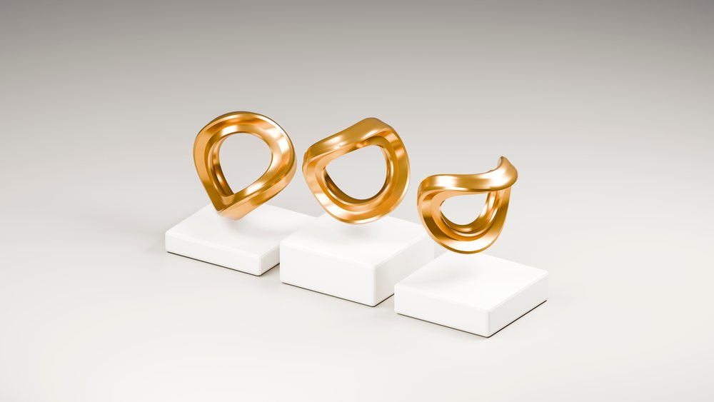 Three abstract golden sculptures with smooth curves each displayed on a white pedestal in a minimalist studio setting.