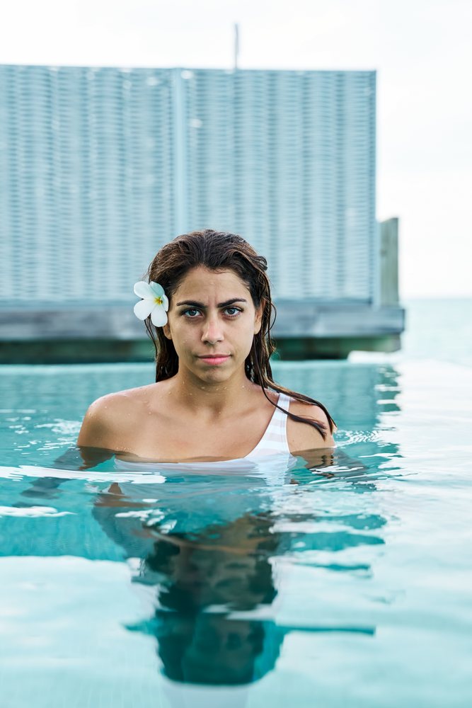 A white woman stands in a swimming pool relaxing during her vacation
